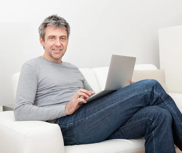 Uomo anziano seduto sul divano e utilizzando il computer portatile — Foto Stock