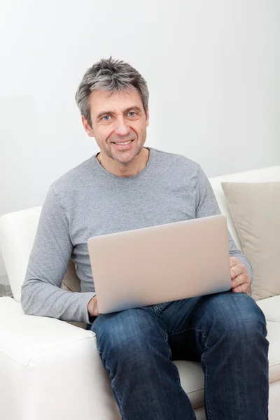 高级的男子坐在沙发和使用的便携式计算机 — 图库照片