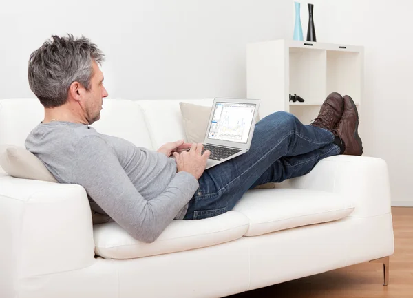 Starszy mężczyzna siedzi w sofę i korzysta z laptopa — Zdjęcie stockowe