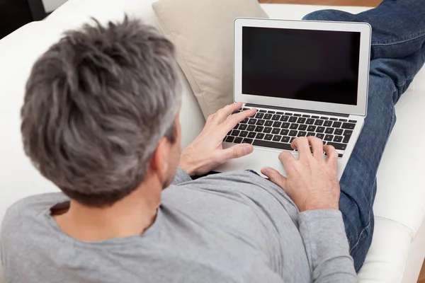 Uomo anziano seduto sul divano e utilizzando il computer portatile — Foto Stock