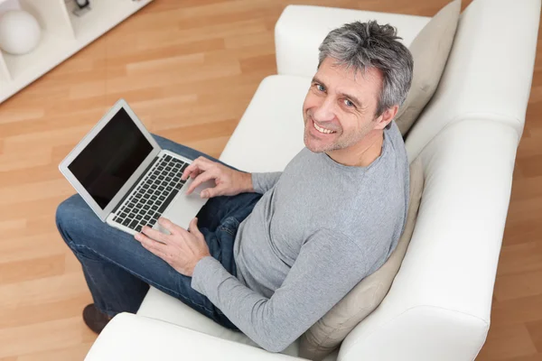 高级的男子坐在沙发和使用的便携式计算机 — 图库照片
