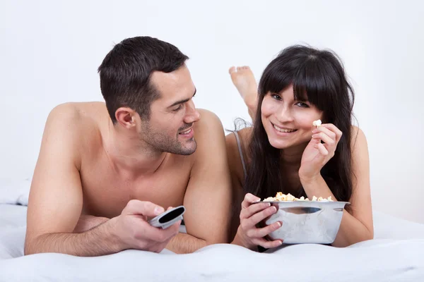 Unga paret ligger i sängen och tittar på tv — Stockfoto