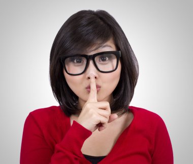 Pretty teenage girl wearing nerd glasses making silence sign clipart