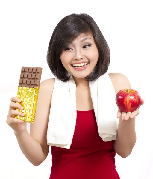 Mujer joven después del ejercicio sosteniendo chocolate y manzana haciendo una elección —  Fotos de Stock