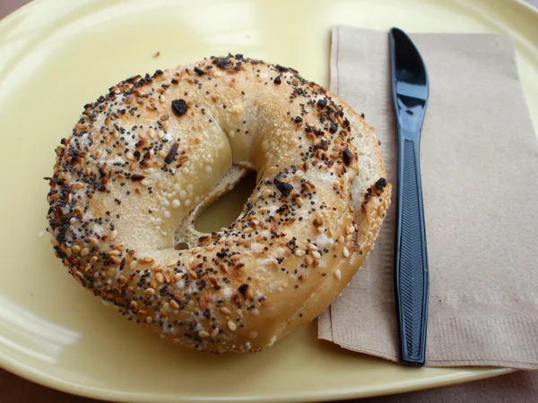 Everything Bagel and Plastic Knife on a yellow plate — Stock Photo, Image
