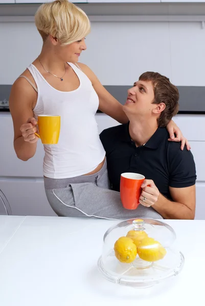 Happy couple posing in the kitchen with cups and lemons — Stock Photo, Image