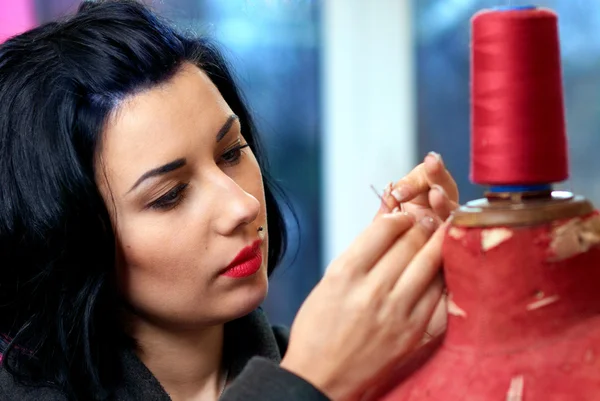 Threading een naaister naald in de buurt van rode oude etalagepop in haar werk — Stockfoto