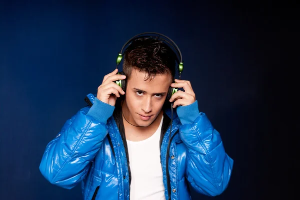 Young man listening music with headphones portrait on blue background — Stock Photo, Image