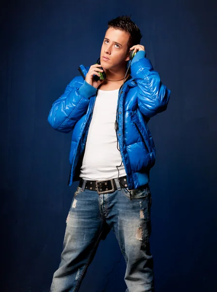 Üzerinde mavi arka plan ayakta kulaklık ile müzik dinleme genç adam — Stok fotoğraf