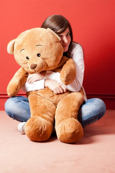 Junge Frau umarmt Teddybär auf dem Boden sitzend Stockfoto