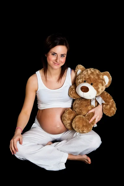 Брюнетка беременная женщина с плюшевым мишкой изолированы на черный — стоковое фото
