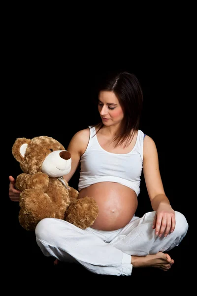 Brunette pregnant woman with teddy bear isolated on black — Stock Photo, Image
