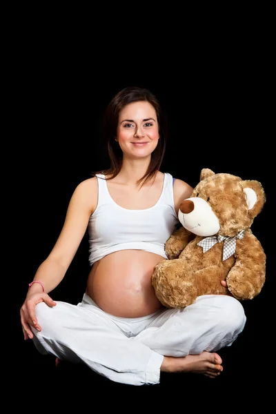 Брюнетка вагітна жінка з ведмедиком ізольовані на чорному — стокове фото