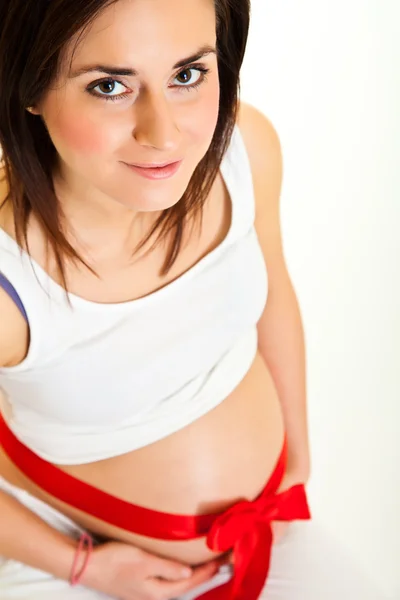 Μελαχρινή γυναίκα έγκυος με κόκκινη κορδέλα που απομονώνονται σε λευκό — Φωτογραφία Αρχείου