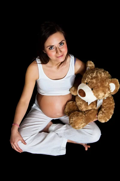 Brunette pregnant woman with teddy bear isolated on black — Stock Photo, Image