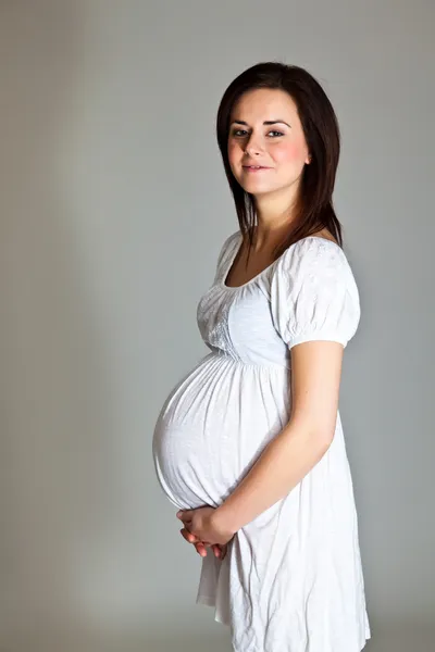 Těhotná bruneta na neutrální pozadí — Stock fotografie