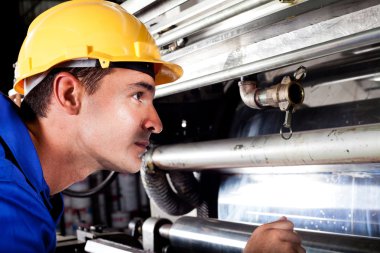 Industrial machine operator checking on machine while it's running clipart