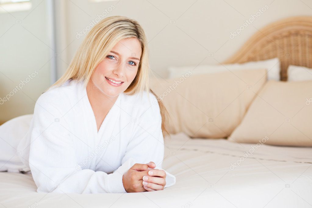 Pretty young woman in bathrobe lying on bed