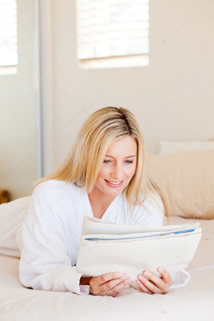 Young woman reading newspaper on bed
