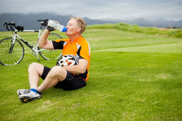 Старший велогонщик принимает брак и питьевую воду — стоковое фото