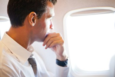Thoughtful businessman on airplane clipart