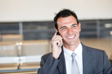 Happy businessman talking on cell phone at airport clipart
