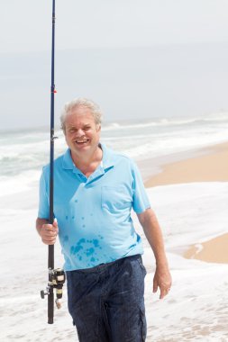 Senior man fishing on beach clipart