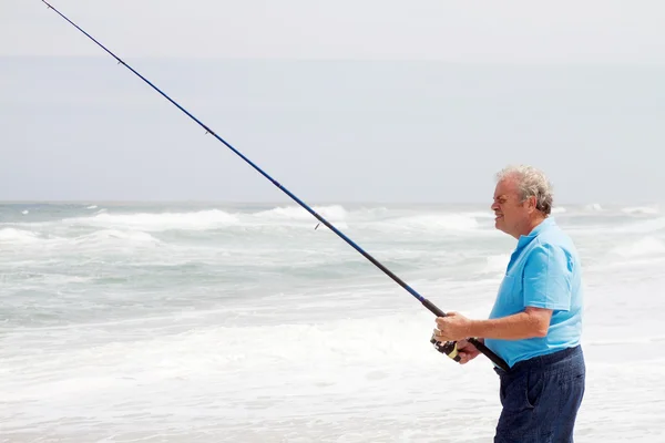 Homem sênior pesca na praia — Fotografia de Stock