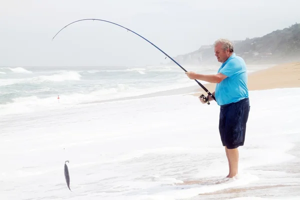 Äldre man fångar fisk på stranden — Stockfoto