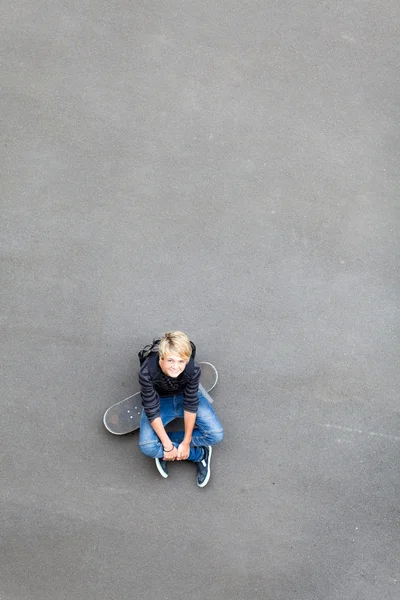 किशोर लड़का स्केटबोर्ड पर बैठे और ऊपर देख रहा है — स्टॉक फ़ोटो, इमेज