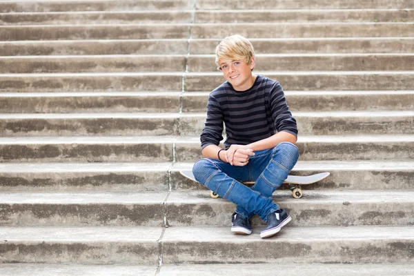 Мальчик-подросток сидит на скейтборде — стоковое фото
