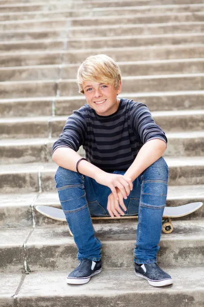 Teen chłopiec siedzi na deskorolce — Zdjęcie stockowe