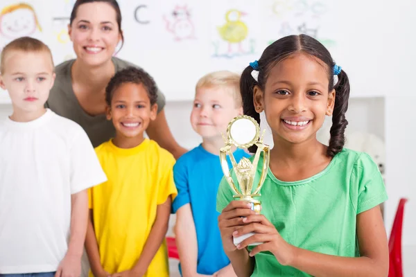 Niña preescolar sosteniendo un trofeo frente a sus compañeros de clase — Foto de Stock