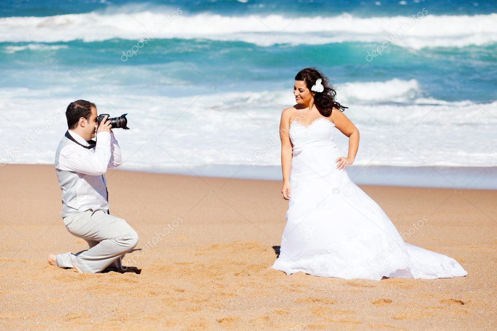 Groom taking bride's photos on beach