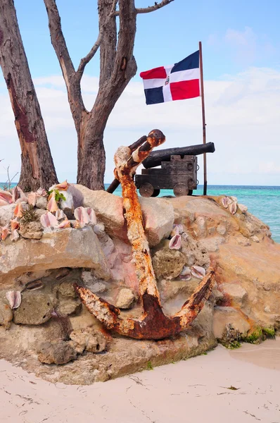 Vecchio cannone in ghisa, e l'ancora della nave davanti alla bandiera della Repubblica Dominicana sulla costa atlantica — Foto Stock