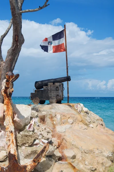 Old cast-iron cannon, and the ship anchor in front of of the flag of the Dominican Republic on the Atlantic coast — Stock Photo, Image