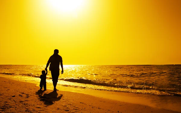 Pai e crianças silhuetas na praia ao pôr do sol — Fotografia de Stock