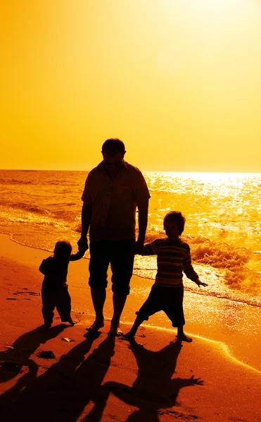 Otce a děti siluety na pláži při západu slunce — Stock fotografie