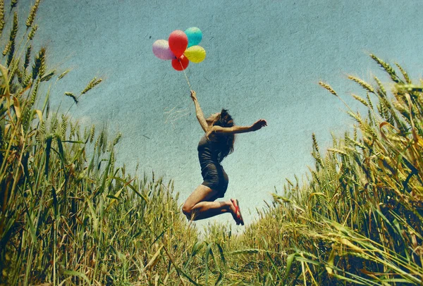 Mladá žena drží barevné balónky a létání přes louku. Foto ve starém stylu obrázek barvy. — Stock fotografie