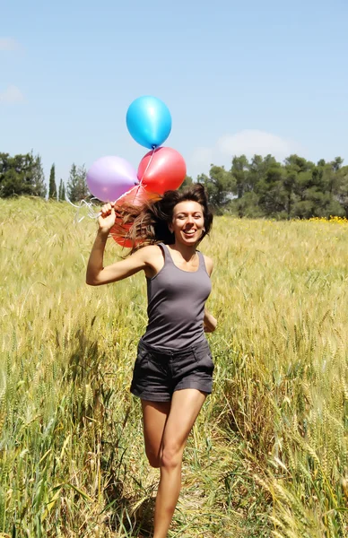 Mujer joven con globos de colores en el campo — Foto de Stock