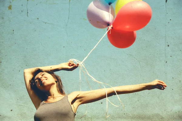 Young woman holding colorful balloons and flying over a meadow. Photo in old color image style. — Stock Photo, Image