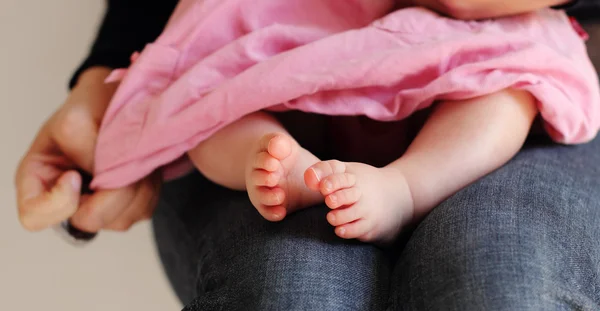 Маленька дівчинка в рожевій сукні сидить на руках матері — стокове фото