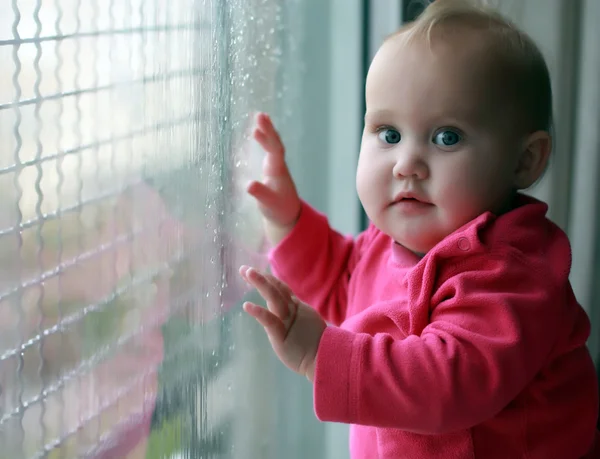 Маленькая девочка смотрит на капли дождя на окне — стоковое фото