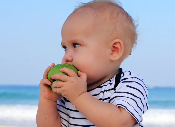Barnet håller ett grönt äpple i bakgrunden havet — Stockfoto