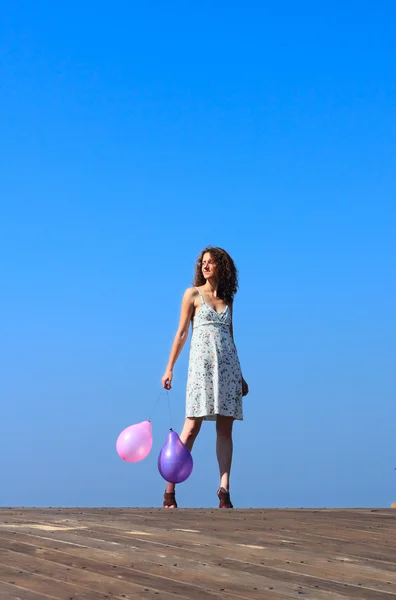 Młoda dziewczyna idzie i fale balony — Zdjęcie stockowe