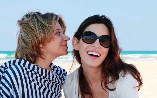 Dos chicas chismorreando. Fondo cielo azul y la playa . — Foto de Stock