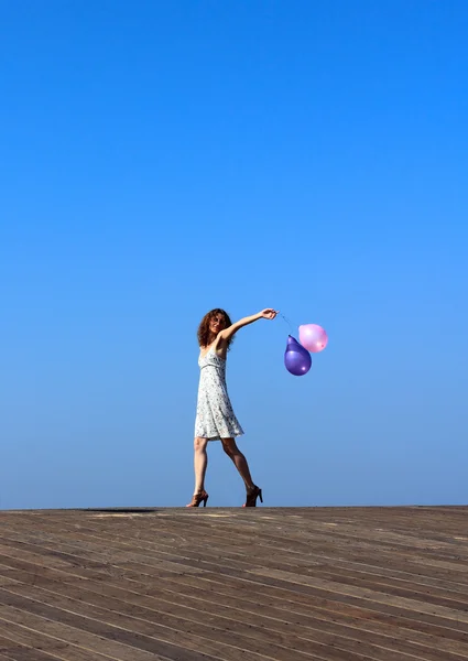 Młoda dziewczyna idzie z balonów na tle błękitnego nieba — Zdjęcie stockowe