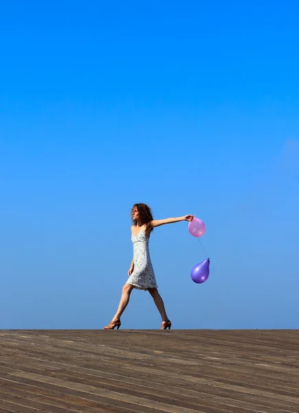 Ung flicka går med ballonger på blå himmel bakgrund — Stockfoto
