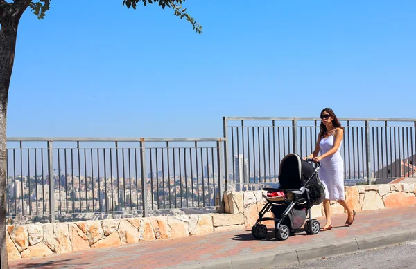 Young mother walking with a stroller on the background of a big — Stock Photo, Image