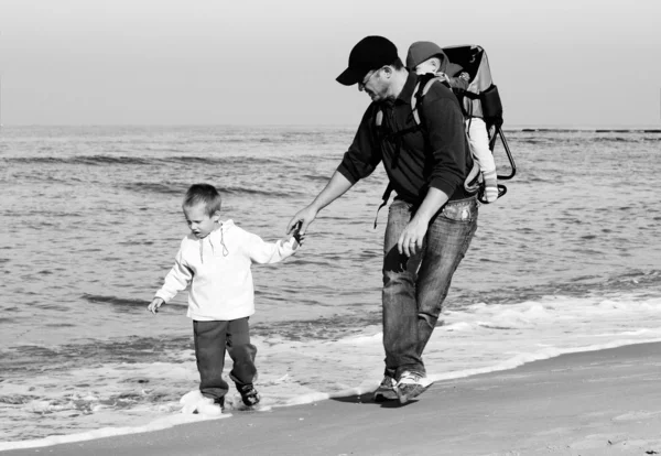 Papá con un niño pequeño caminando en una playa de invierno . — Foto de Stock